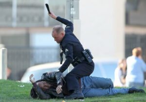 Uniformed police officer restrains a man on the grass in an urban area, during an arrest.